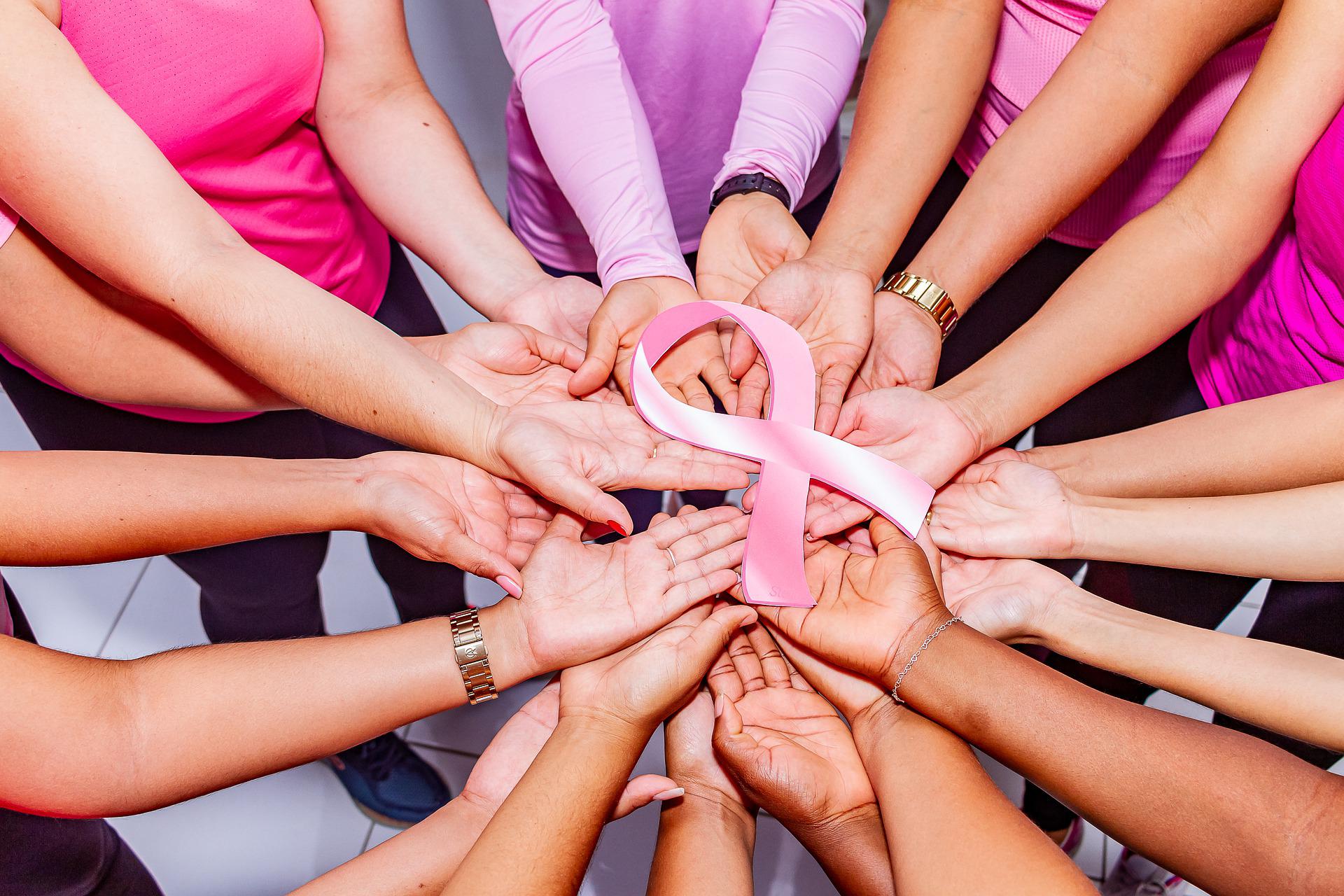 Circle of hands, palms up, with a pink ribbon in the center, signifying unity and women's health.