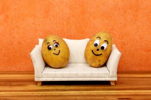 Two potatoes with eyes, nose and mouth sitting on a couch to illustrate the term couch potatoes
