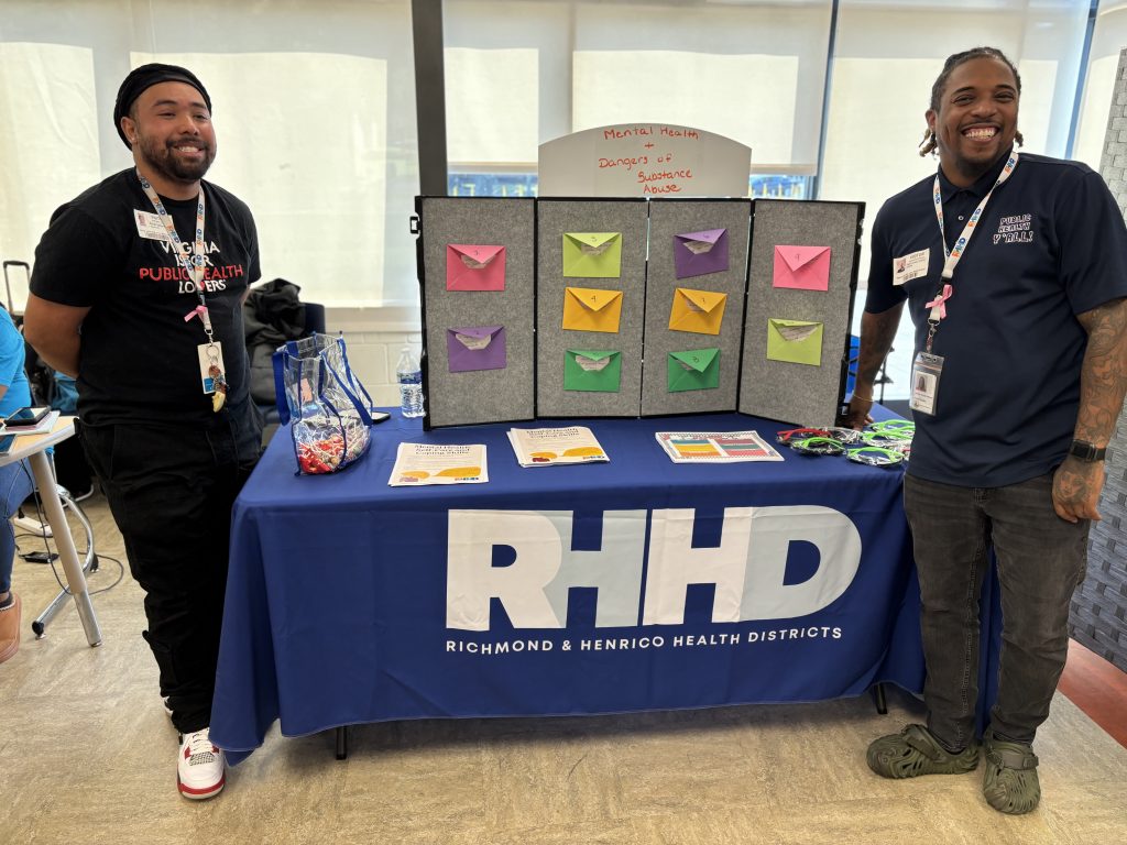 Two people standing with an RHHD table at an outreach event