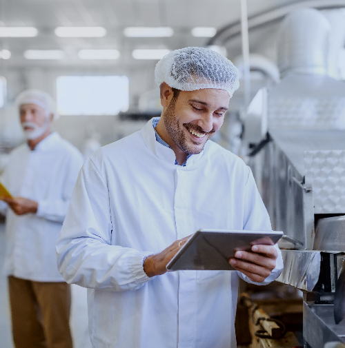 A smiling man in a kitchen wearing a hairnet and holding a tablet computer