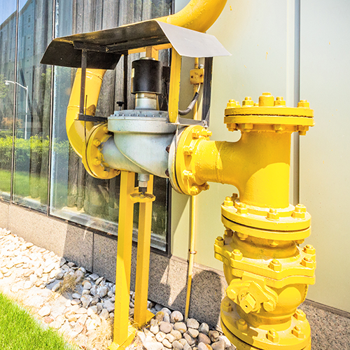 A large yellow pipe coming out of the ground along side a building