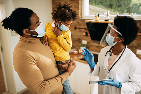Un hombre sostiene a su hijo mientras el médico les habla. Todos con mascarillas quirúrgicas para evitar la propagación del covid