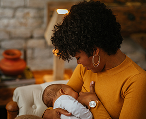 Black woman nurses her newborn baby while sitting on sofa at home