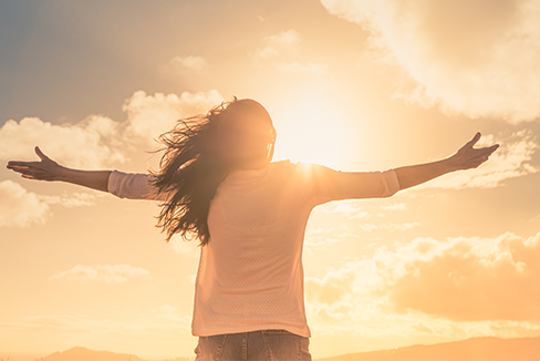 Woman with arms outstretched in front of a sunrise