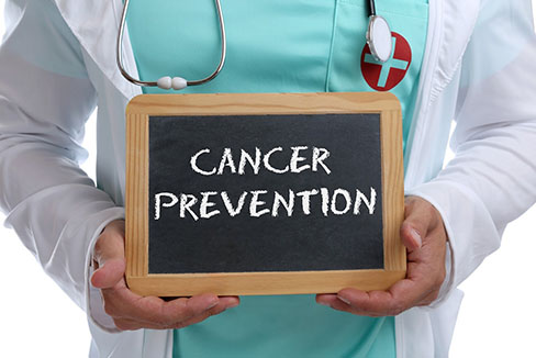 médico masculino que sostiene un estetoscopio que sostiene un letrero de pizarra que tiene "PREVENCIÓN DEL CÁNCER" escrito con tiza