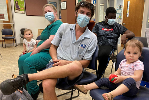 several adults and children in face masks awaiting their COVID-19 vaccines