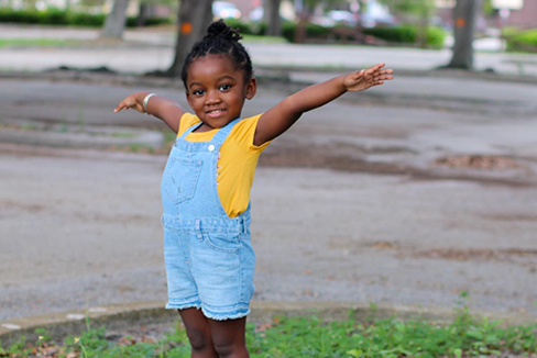 little girl standing on curb with arms outstretched 