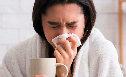 Foto de una mujer vestida con una bata mientras se sona la nariz con un pañuelo.
