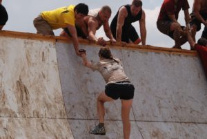 woman being helped over wall by teammates