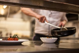 Person preparing food at a work station, head obscured