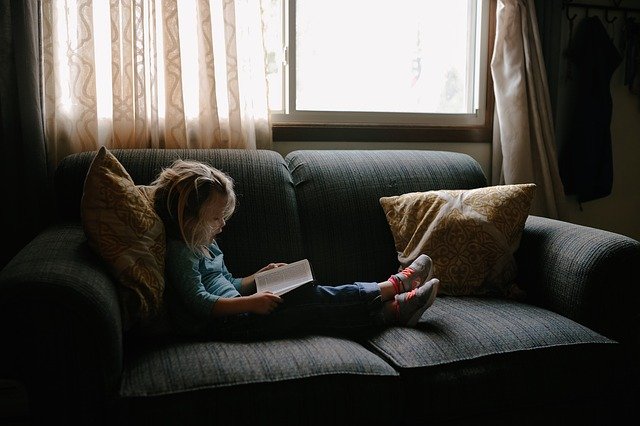 Image of blond child reading on a couch with throw pillows