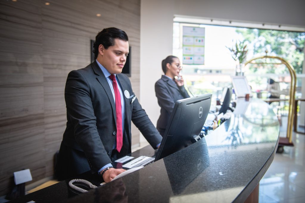 male receptionist at hotel lobby desk looking at computer