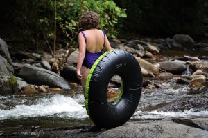 A girl standing in bathing suit with tube looking at river rapids