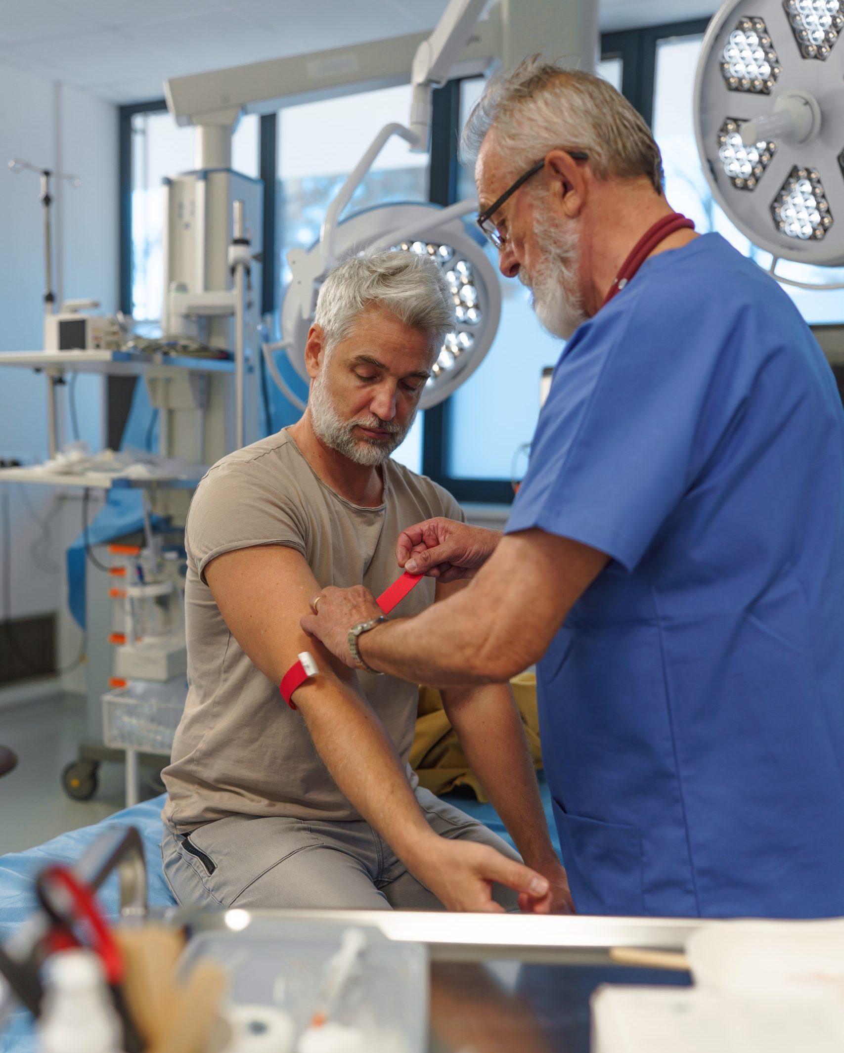 Older doctor drawing blood from patient's arm during medical examination.