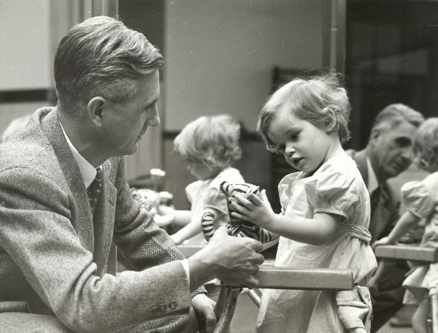 Image of Mack Shanholtz, 1951 VDH Commissioner giving a stuffed toy tiger to a young girl in leg braces with a walker