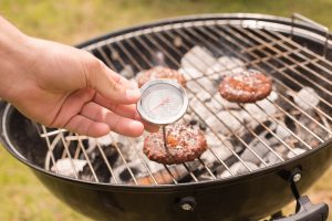 Man using meat thermometer while barbecuing on a sunny day