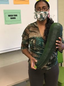 Photo of Healthy Harvest Community Garden staff member holding a large zucchini