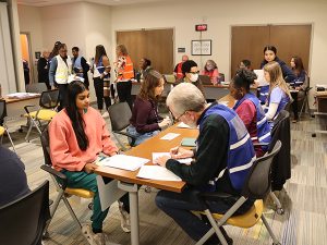 People sit at a table with others in the background standing.