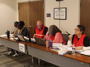 People in red and tan vests sit at a table labeled Controller Area.