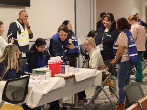 People crowd around a table with a red sharps container.
